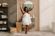 © gstockstudio - Full length of playful plus size African woman covered in towel dancing in domestic bathroom