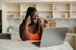 © gstockstudio - Happy plus size African woman talking on mobile phone and using laptop while working at home