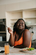 © gstockstudio - Happy curvy African woman enjoying healthy food for lunch at the domestic kitchen