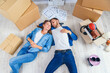 © gorynvd - Happy young caucasian couple lying down on the wooden floor while having a break while moving to new house. Top view.