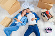 © gorynvd - Happy young caucasian couple lying down on the wooden floor while having a break while moving to new house. Top view.