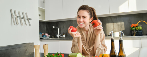 Wall Mural - Portrait of beautiful woman cooking in the kitchen, chopping vegetables on board, holding tomatoes, lead healthy lifestyle with preparing fresh salads, vegan meals