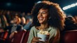 young dark-skinned woman sitting in cinema hall holding bucket of popcorn smiling and looking cheerfully into the camera, eyes and mouth wide open, enjoying and having fun at the movie theater