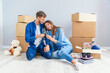 © gorynvd - Couple taking a break on moving day, sitting on floor in new apartment celebrating with champagne surrounded by cardboard boxes.