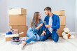© gorynvd - Couple taking a break on moving day, sitting on floor in new apartment celebrating with champagne surrounded by cardboard boxes.