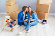 © gorynvd - Couple taking a break on moving day, sitting on floor in new apartment celebrating with champagne surrounded by cardboard boxes.