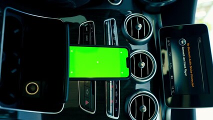 vertical video close-up of a phone with a green screen display stands on the dashboard in a luxurious auto connection technology