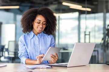 Young successful woman working with tablet computer inside office at workplace, smiling female programmer testing new app, writing code for software