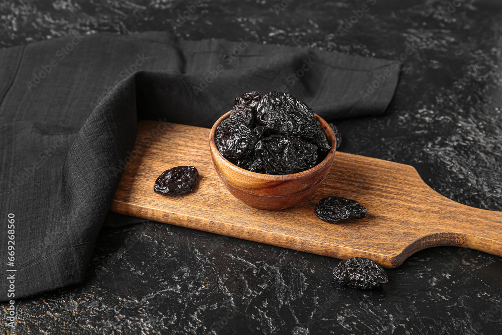Bowl with tasty prunes and cutting board on black grunge table