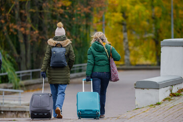 Two women with suitcases traveling around Europe in late autumn walking on pathway