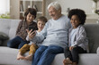 © fizkes - Elderly great-grandfather and three little great-grandchildren having fun with smart phone watch funny videos, enjoy new amusing mobile application at home. Multi-generational people using modern tech