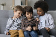 © fizkes - Three kids using smartphone together sitting on sofa, spend free time at home have fun with device, play cool new on-line games, friendly brothers watch funny videos in social network, browse internet
