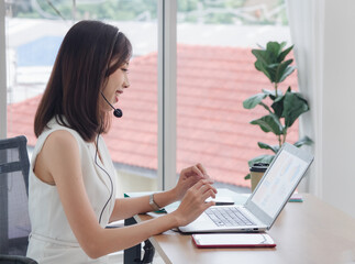 Wall Mural - Portrait woman Asian one person wearing white dress, pretty girl smile sitting chair on desk looking notebook ready for business service call center working job online sale inside the room office