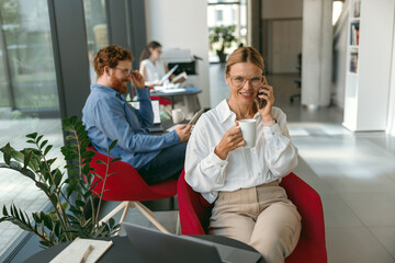 Wall Mural - Businesswoman talking on phone with client while working on laptop in office . High quality photo