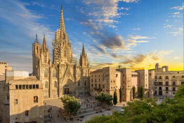 View of the Gothic Barcelona Cathedral of the Holy Cross and Saint Eulalia with surround buildings, plaza and the skyline of Barcelona in view as the sun sets at dusk.