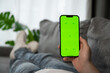 Man lying on the sofa with smartphone in his hands with green chroma screen. Food delivery app,online shopping etc