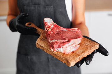 Wall Mural - Butcher woman prepare fresh raw meat pork entrecote steak on wooden board, top view on dark background