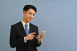 © saltdium - Waist up portrait of Young Asian man in formal suit using mobile phone on color isolated studio background