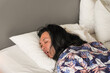 © Rizky - Long haired asian man is sleeping with prone position and his mouth open on a bed with a white pillow. Unusual sleep posture at the hotel during holiday vacation. Rest after a long journey