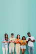 © Jose Calsina - Vertical. Multiracial group of young friends smiling using their mobile phone app at teal wall. Teenagers having fun sharing messages on social media with a cellphone at blue color background. High