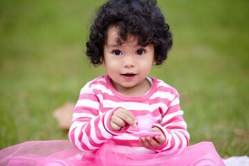 Canvas Print - Nature, portrait and girl kid in a garden play with toy on the grass on summer weekend. Adorable, playful and young child, baby or toddler with curly hair sitting on the lawn in outdoor field or park