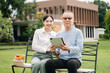 © laddawan - Happy adult granddaughter and senior grandfather having fun enjoying talk while relaxing sitting outdoor in park..