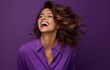 A radiant woman in a purple shirt laughs wholeheartedly against a complementary purple backdrop. Ideal for representing positivity, beauty, and genuine emotion in marketing or editorial content.