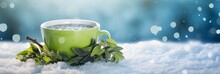 Green Tea Cup With Mint Leaves On Snowy Surface. Blurred Winter Background. Christmas And New Year. Suitable For Holiday Greetings, Promotions, Or Banner With Free Space For Text
