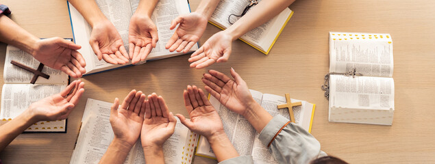 Wall Mural - Cropped image of diversity people hand praying together at wooden church on bible book. Group of believer hold hand together faithfully. Concept of hope, religion, faith, god blessing. Burgeoning.