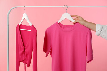 Wall Mural - Woman taking stylish t-shirt from rack on pink background, closeup
