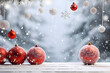 Red Christmas balls hanging and standing on white wooden board ground covered with snow with abstract spruce trees and snowfall in the background.