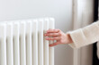 Woman in sweater warming her hands at heating radiator close up