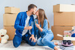 © gorynvd - Couple taking a break on moving day, sitting on floor in new apartment celebrating with champagne surrounded by cardboard boxes.