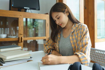 Wall Mural - Education and literacy concept, College student girl reading textbook and taking notes on notebook