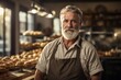 © Igor - bearded senior male baker in uniform and apron standing at counter in bakery. ai generative