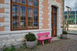 Eine kleine, pinkfarbene Sitzbank vor einer Mauer mit Eingangstür und grossem Fenster am Bahnhof von Toblach im Pustertal in Südtirol