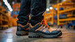 © PaulShlykov - Close-up safety working shoe on a worker feet is standing at the factory, ready for working in danger workplace concept. Industrial working scene and safety equipment.