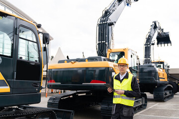 Aufkleber - Engineer in a helmet with a digital tablet stands next to construction excavators.