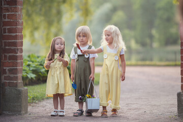 Two girls and boy walking in the summer park with flowers 