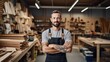 A carpenter stands with his arms crossed in his woodworking shop looking at the camera.