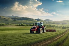 The Tractor Is Driving Through A Green Field, Cultivating The Land Against The Background Of The Sky And The Landscape With Mountains. Agricultural Machinery In The Field. Farmer's Land.