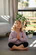 © Виктория Попова - A cute girl is sitting in a yoga pose and meditating with her eyes closed, sitting on the floor. Yoga for children.