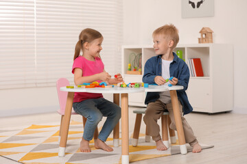 Wall Mural - Little children playing with wooden pieces and string for threading activity at white table indoors. Developmental toys