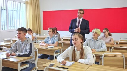 Wall Mural - Positive teacher helping teenage schoolchildren during lesson in schoolroom