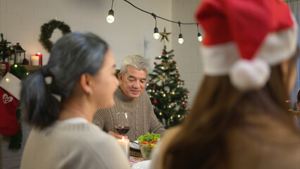 Happy asian family celebrating Christmas together at home. Cheerful senior parents and children in Santa hat clinking glasses of red wine.