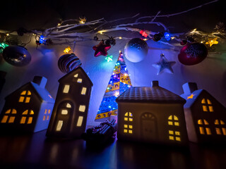 Wall Mural - christmas home decorations. toy white houses with burning lights inside and twig with glowing garland lights and glass balls.