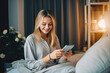 © VisualProduction - Beautiful young woman using mobile phone while relaxing in bed before bedtime, checking social media before going to sleep