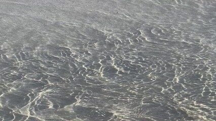 Wall Mural - Top view of a sea-wave come and removing a footprint on a wet sand on the beach on a sunny day