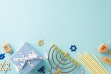 Jewish Tradition: Overhead View Of Menorah, Star Of David Symbols, Gift Box With Bow, Candles, And Dreidel On A Soft Blue Surface—ideal For Your Text Or Advertisement