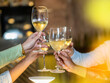 © Lomb - A close-up of friends raising their glasses in a toast, celebrating with chilled white wine. The golden hue from the ambiance emphasizes the warmth of the gathering.